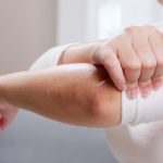 Young woman having pain in her elbow and using hand for self-massage to relieve aches and pains.